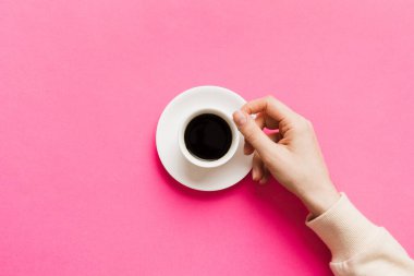 Renkli arka planda bir fincan kahve tutan minimalist stil bir kadın. Düz yatıyordu, üstten espresso fincanı. Metin için boş yer, kopyalama alanı. Kahve bağımlılığı. Üst manzara, düz uzanma.