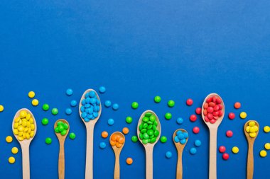 Renkli arka planda kaşık üzerinde renkli tatlı şekerler. Fotokopi alanı ile şekerleme dekoru üst görünümü.