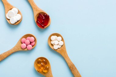 Renkli bir arka planda kaşıkta vitamin kapsülleri. Haplar sağlıklı bir yemek olarak sunuldu. Kırmızı yumuşak jel vitamin takviye kapsülleri kaşık üzerinde.