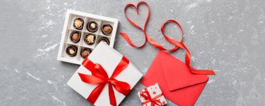 Sevgililer Günü için renkli arka planda hediye kutusu ve çikolatalı zarf. Kalp, hediye kutusuyla şekillendirilmiş çikolatalar fotokopi alanı ile üst görünüm.