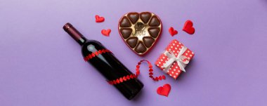 Sevgililer Günü için renkli arka planda bir şişe kırmızı şarap hediye ve çikolatalı. Kalp, hediye kutusuyla şekillendirilmiş çikolatalar fotokopi alanı ile üst görünüm.