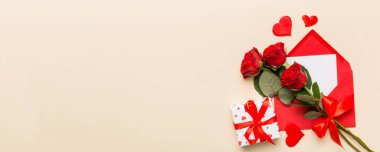 Zarflı sevgililer günü kompozisyonu, gül çiçeği ve kırmızı kalp masada. Üst manzara, düz yatış. Tatil kavramı.