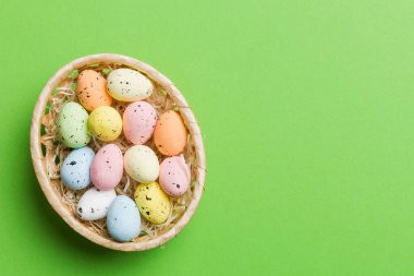 Colorful Easter eggs in wicker basket against colored background, closeup. top view with copy space.