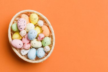 Colorful Easter eggs in wicker basket against colored background, closeup. top view with copy space.