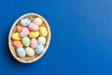 Colorful Easter eggs in wicker basket against colored background, closeup. top view with copy space.