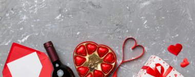 Sevgililer Günü için renkli arka planda bir şişe kırmızı şarap hediye kutusu, zarf ve çikolatalı. Kalp, hediye kutusuyla şekillendirilmiş çikolatalar fotokopi alanı ile üst görünüm.