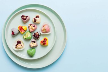 Plate with different chocolate on colored background. Assortment of fine chocolates top view vith copy space Health and obesity concept.