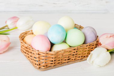 Mutlu Paskalya kompozisyonu. Renkli masada sarı laleli sepetli Paskalya yumurtaları. Fotokopi alanı olan doğal renkli yumurtalar.