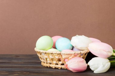 Mutlu Paskalya kompozisyonu. Renkli masada sarı laleli sepetli Paskalya yumurtaları. Fotokopi alanı olan doğal renkli yumurtalar.