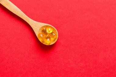 Renkli bir arka planda kaşıkta vitamin omega kapsülleri. Haplar sağlıklı bir yemek olarak sunuldu. Kırmızı yumuşak jel vitamin takviye kapsülleri kaşık üzerinde.