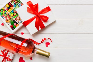 Sevgililer Günü için renkli arka planda bir şişe kırmızı şarap hediye ve çikolatalı. Kalp, hediye kutusuyla şekillendirilmiş çikolatalar fotokopi alanı ile üst görünüm.