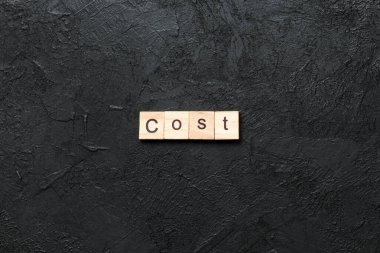 Ahşap blokta yazılmış bir kelime. Masada maliyet metni, konsept.