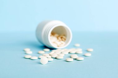 Medicine bottle and white pills spilled on a light background. Medicines and prescription pills flat lay background. White medical pills and tablets spilling out of a drug bottle.
