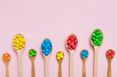 Renkli arka planda kaşık üzerinde renkli tatlı şekerler. Fotokopi alanı ile şekerleme dekoru üst görünümü.