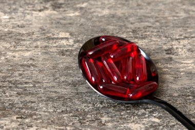 Renkli bir arka planda kaşıkta vitamin kapsülleri. Haplar sağlıklı bir yemek olarak sunuldu. Kırmızı yumuşak jel vitamin takviye kapsülleri kaşık üzerinde.