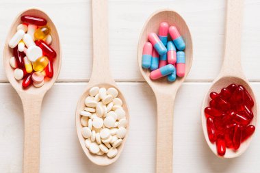 Renkli bir arka planda kaşıkta vitamin kapsülleri. Haplar sağlıklı bir yemek olarak sunuldu. Kırmızı yumuşak jel vitamin takviye kapsülleri kaşık üzerinde.