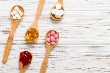 Renkli bir arka planda kaşıkta vitamin kapsülleri. Haplar sağlıklı bir yemek olarak sunuldu. Kırmızı yumuşak jel vitamin takviye kapsülleri kaşık üzerinde.