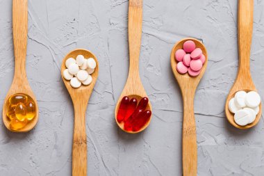 Renkli bir arka planda kaşıkta vitamin kapsülleri. Haplar sağlıklı bir yemek olarak sunuldu. Kırmızı yumuşak jel vitamin takviye kapsülleri kaşık üzerinde.