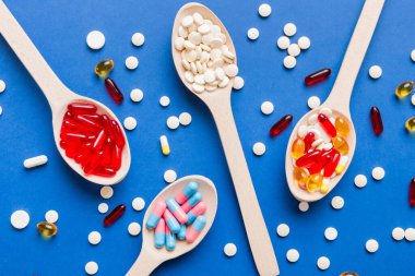 Renkli bir arka planda kaşıkta vitamin kapsülleri. Haplar sağlıklı bir yemek olarak sunuldu. Kırmızı yumuşak jel vitamin takviye kapsülleri kaşık üzerinde.