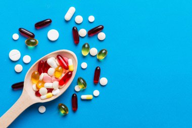 Renkli bir arka planda kaşıkta vitamin kapsülleri. Haplar sağlıklı bir yemek olarak sunuldu. Kırmızı yumuşak jel vitamin takviye kapsülleri kaşık üzerinde.