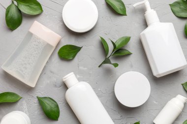 Çimento arka planında yeşil yaprakları olan organik kozmetik ürünler. Düz yatıyordu.