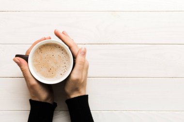 Renkli arka planda bir fincan kahve tutan minimalist stil bir kadın. Düz yerde, kapuçino bardağının üstünde. Metin için boş yer, kopyalama alanı. Kahve bağımlılığı. Üst manzara, düz uzanma.