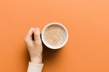 Renkli arka planda bir fincan kahve tutan minimalist stil bir kadın. Düz yerde, kapuçino bardağının üstünde. Metin için boş yer, kopyalama alanı. Kahve bağımlılığı. Üst manzara, düz uzanma.