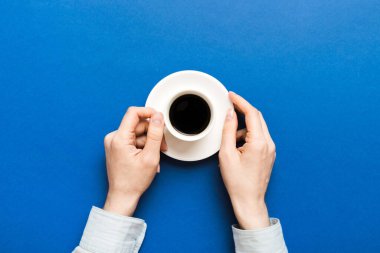 Renkli arka planda bir fincan kahve tutan minimalist stil bir kadın. Düz yerde, kapuçino bardağının üstünde. Metin için boş yer, kopyalama alanı. Kahve bağımlılığı. Üst manzara, düz uzanma.