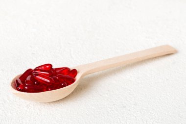 Renkli bir arka planda kaşıkta vitamin kapsülleri. Haplar sağlıklı bir yemek olarak sunuldu. Kırmızı yumuşak jel vitamin takviye kapsülleri kaşık üzerinde.