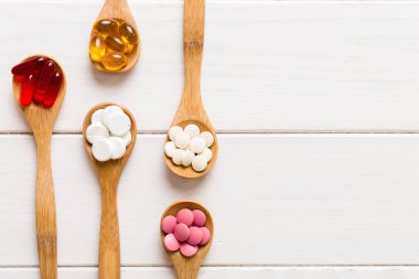 Renkli bir arka planda kaşıkta vitamin kapsülleri. Haplar sağlıklı bir yemek olarak sunuldu. Kırmızı yumuşak jel vitamin takviye kapsülleri kaşık üzerinde.