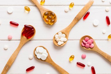 Renkli bir arka planda kaşıkta vitamin kapsülleri. Haplar sağlıklı bir yemek olarak sunuldu. Kırmızı yumuşak jel vitamin takviye kapsülleri kaşık üzerinde.