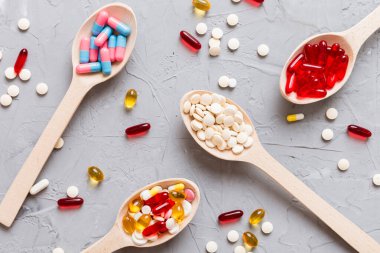 Renkli bir arka planda kaşıkta vitamin kapsülleri. Haplar sağlıklı bir yemek olarak sunuldu. Kırmızı yumuşak jel vitamin takviye kapsülleri kaşık üzerinde.