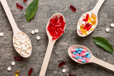 Renkli bir arka planda kaşıkta vitamin kapsülleri. Haplar sağlıklı bir yemek olarak sunuldu. Kırmızı yumuşak jel vitamin takviye kapsülleri kaşık üzerinde.