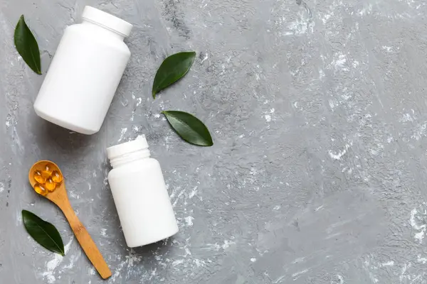 Omega-3 kapsülleri yeşil yapraklı arka planda beyaz bir şişede yatar. Balık yağı tabletleri. Biyolojik olarak aktif katkı maddeleri. Omega 6, Omega 9, A vitamini, E, D vitamini, D3 vitamini..