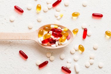 Renkli bir arka planda kaşıkta vitamin kapsülleri. Haplar sağlıklı bir yemek olarak sunuldu. Kırmızı yumuşak jel vitamin takviye kapsülleri kaşık üzerinde.