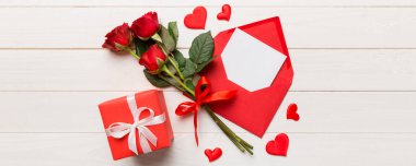 Zarflı sevgililer günü kompozisyonu, gül çiçeği ve kırmızı kalp masada. Üst manzara, düz yatış. Tatil kavramı.