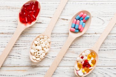 Renkli bir arka planda kaşıkta vitamin kapsülleri. Haplar sağlıklı bir yemek olarak sunuldu. Kırmızı yumuşak jel vitamin takviye kapsülleri kaşık üzerinde.