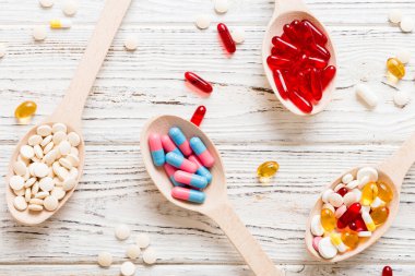 Renkli bir arka planda kaşıkta vitamin kapsülleri. Haplar sağlıklı bir yemek olarak sunuldu. Kırmızı yumuşak jel vitamin takviye kapsülleri kaşık üzerinde.