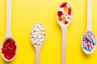 Renkli bir arka planda kaşıkta vitamin kapsülleri. Haplar sağlıklı bir yemek olarak sunuldu. Kırmızı yumuşak jel vitamin takviye kapsülleri kaşık üzerinde.