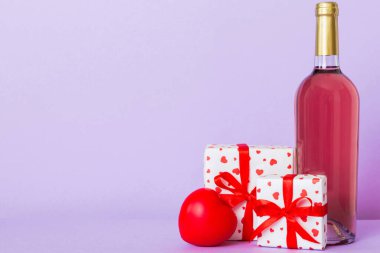 Bottle of wine on colored background for Valentine Day with gift box. Heart shaped with presrnt box perspective view with copy space.
