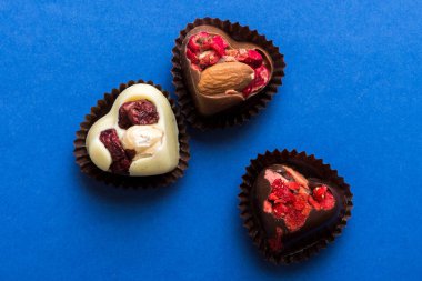 chocolate sweets in the form of a heart with fruits and nuts on a colored background. top view with space for text, holiday concept.