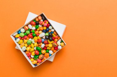 Renkli bir arka planda saten bir kurdeleyle karton kutuda farklı şekerler. Tatil kavramı.