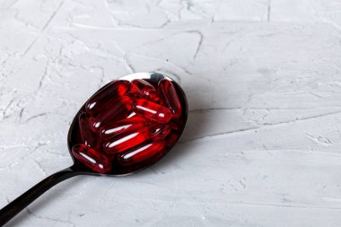 Renkli bir arka planda kaşıkta vitamin kapsülleri. Haplar sağlıklı bir yemek olarak sunuldu. Kırmızı yumuşak jel vitamin takviye kapsülleri kaşık üzerinde.