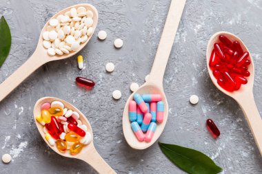 Renkli bir arka planda kaşıkta vitamin kapsülleri. Haplar sağlıklı bir yemek olarak sunuldu. Kırmızı yumuşak jel vitamin takviye kapsülleri kaşık üzerinde.