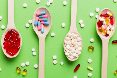 Renkli bir arka planda kaşıkta vitamin kapsülleri. Haplar sağlıklı bir yemek olarak sunuldu. Kırmızı yumuşak jel vitamin takviye kapsülleri kaşık üzerinde.