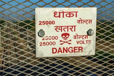 25 bin voltluk tehlike işareti Pune India yakınlarındaki bir köprüden geçiyor. Bu tür işaretler Hindistan 'daki elektrikli demiryolu bölümlerinin üzerindeki köprülere rutin olarak konur..
