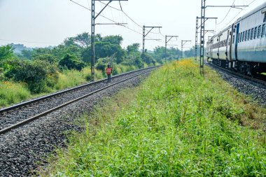 Pune, Hindistan - 08 Ekim 2023: Tren raylarında yürüyen bir demiryolu çetesi üyesi Pune Hindistan yakınlarındaki bitişik raylardan geçerken,.