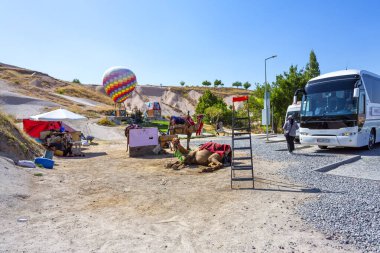 GOREME, TURKYE 2023, Ağustos 07: Fotoğraf Uchisar köyünün girişi, tur otobüsü, deve ve ve sıcak hava balonunun önünde çekildi