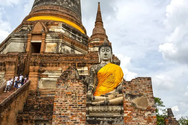 Sarı kumaşa sarılı huzurlu bir Buda heykeli tuğla kalıntılarının arasında duruyor ve Tayland 'ın Ayutthaya kentinde Wat Yai Chai Mongkhon' lu Chedi