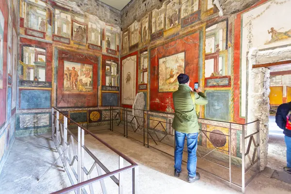 Ziyaretçiler, İtalya 'nın Pompei kentindeki arkeoloji sahasındaki Vettii Hanesi' nin duvarlarında mitolojik sahneler ve günlük yaşamı tasvir eden canlı ve iyi korunmuş fresklere hayranlık duyuyorlar.